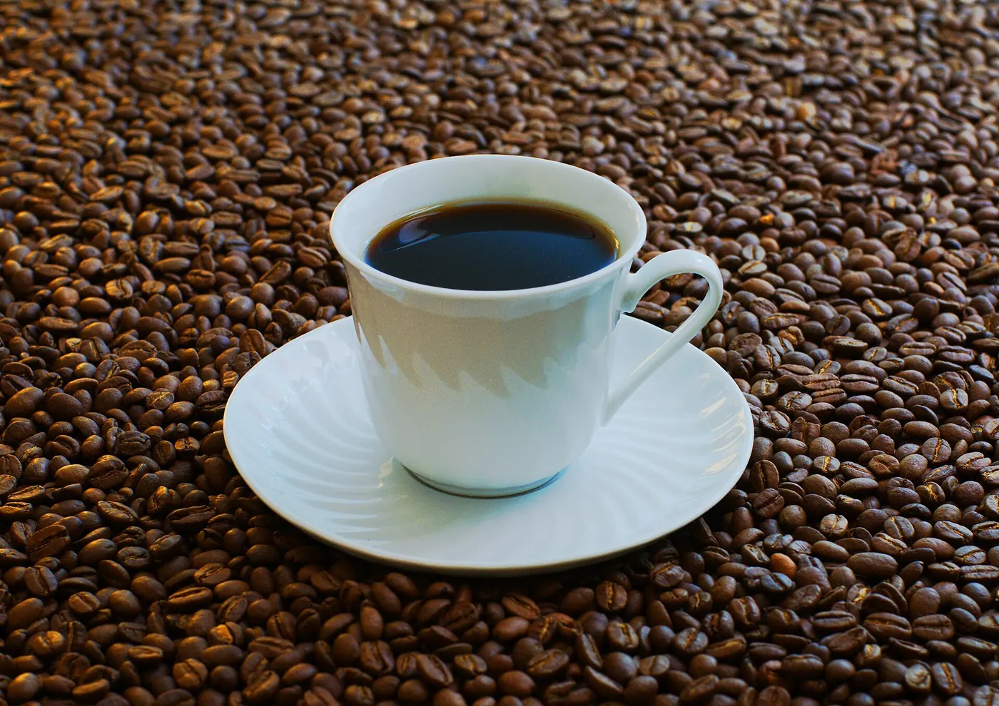 A cup of black coffee on a bed of roasted beans