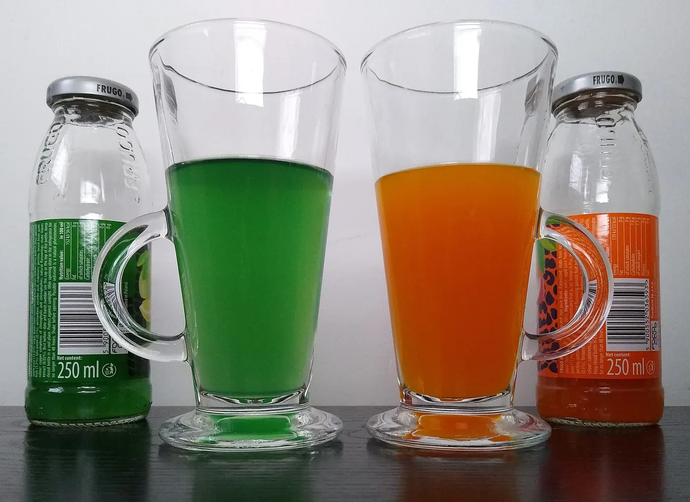 Glasses of bright green and orange soft drinks